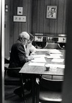 Black and white photograph of the reading room at the Leo Goodwin Institute for Cancer Research. Portrait on the far wall is of Dr. James Reyniers, founder of the Lobund Institute originally located at the University of Notre Dame. Claire Thunning Ph.D. student is sitting at the reading room table next to an unidentified man